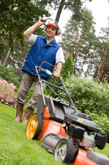 A man mowing a hilly lawn with a lawn mower and a safety helmet