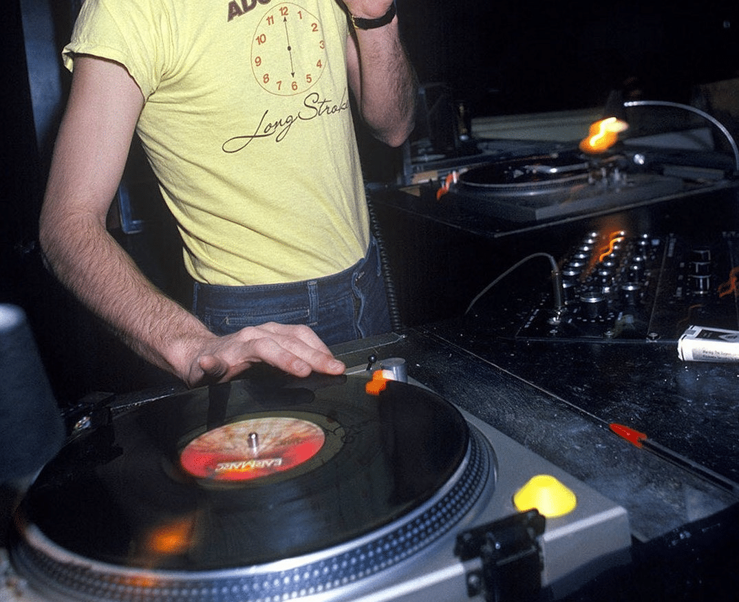 A person playing a vinyl record on a turntable, with a stack of records nearby
